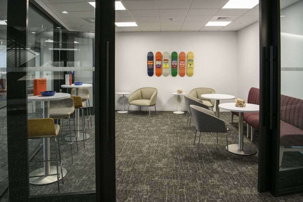 Casual conference space including high and low tables, chairs and bench seating, and colorful artwork of Campbells soup pop art painted on skateboards.