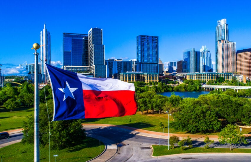 The Texas state flag flies in front of the skyline of Austin.