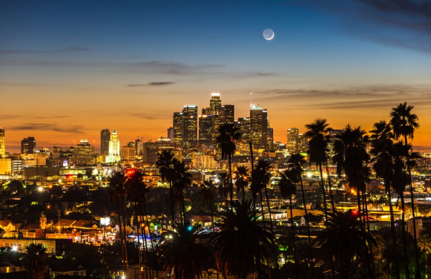 Los Angeles skyline at dusk with the moon overhead.