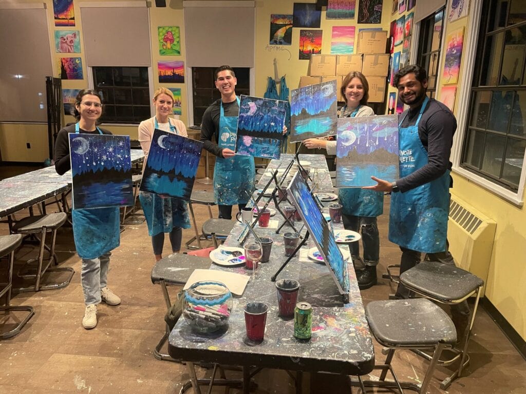 Five summer associates and guides holding up their completed paintings after a paint-and-sip event in San Diego.
