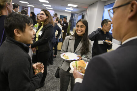 Two male attorneys with backs to the camera talking with smiling female Life Sciences Scholar at welcome reception.